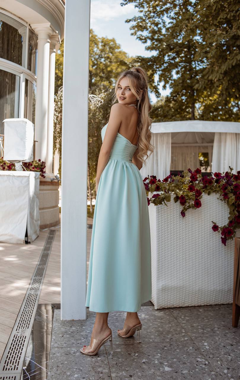 Woman in a light blue dress standing outdoors near a white building with greenery.