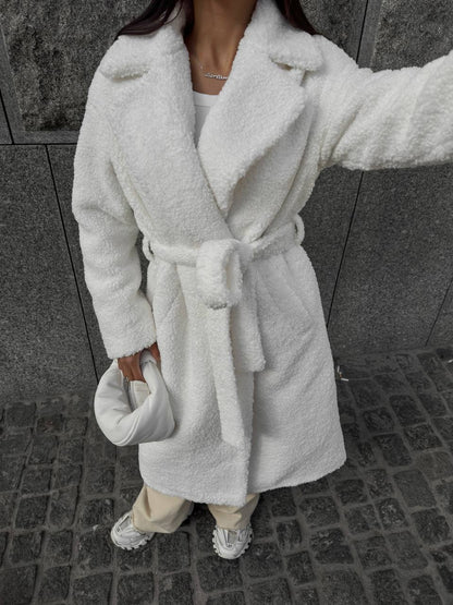 Person wearing a white plush robe on a stone pavement.