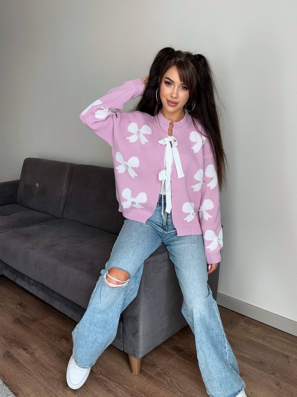 Woman wearing a pink sweater with white patterns and blue jeans in a room.