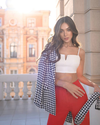 Woman wearing a white top and red pants with a black and white checkered scarf in an outdoor setting.