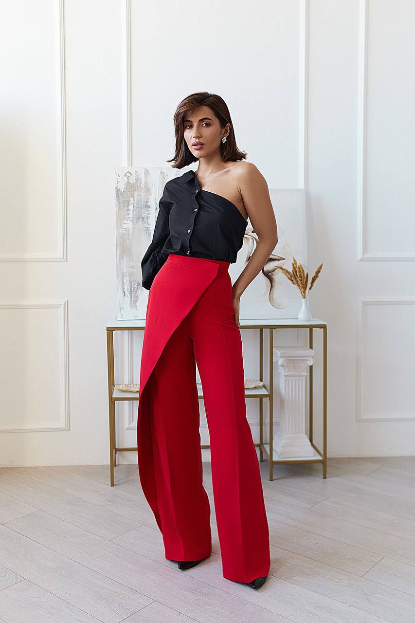 Woman wearing a black top and red pants in a minimalistic room.
