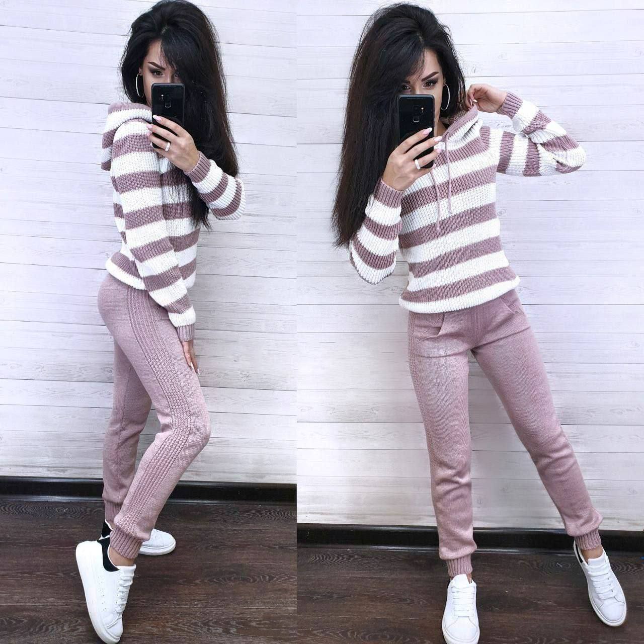 Woman wearing a striped sweater and pink pants standing against a white wall.