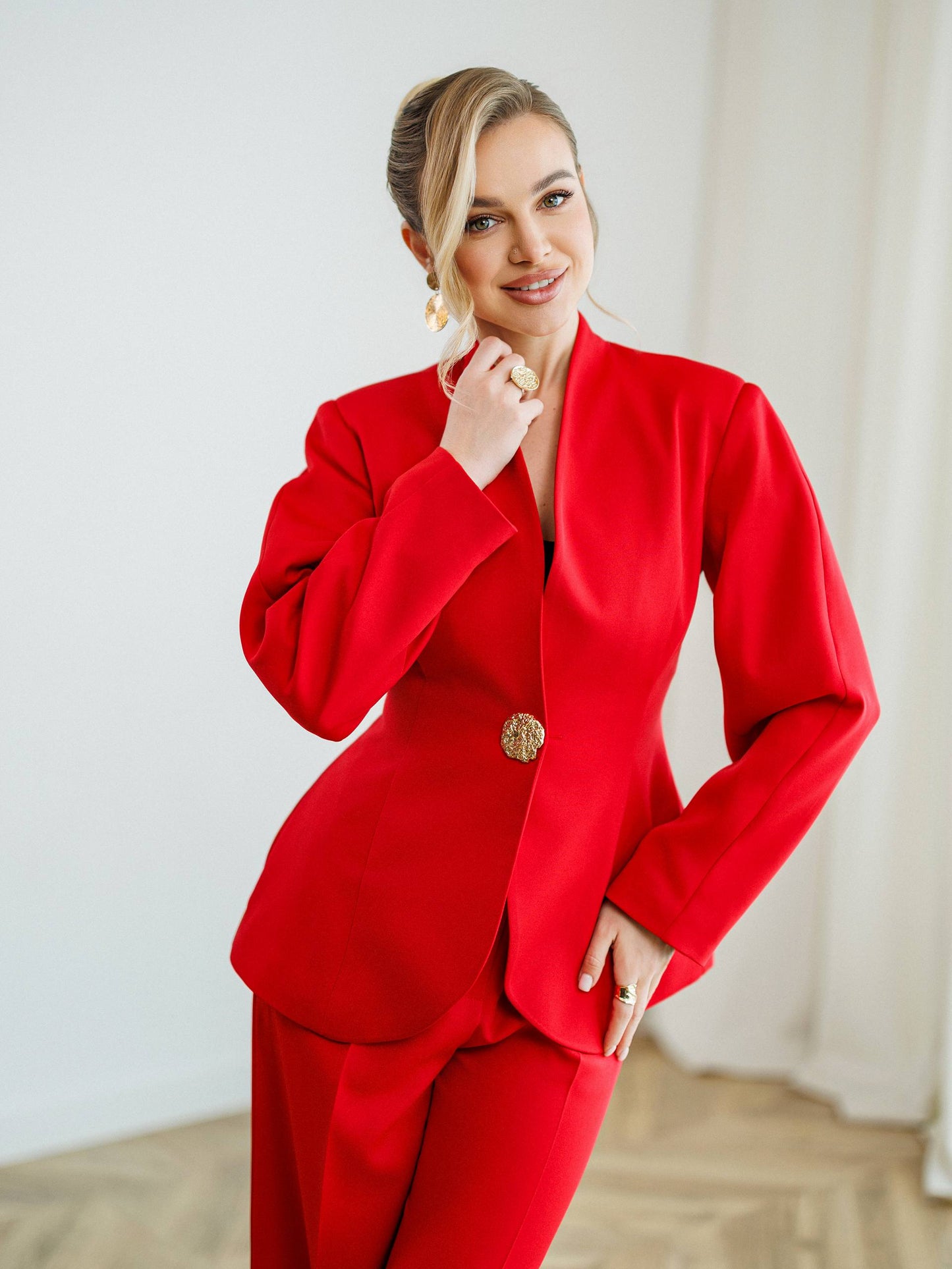 Woman wearing a red suit with a gold button against a white background