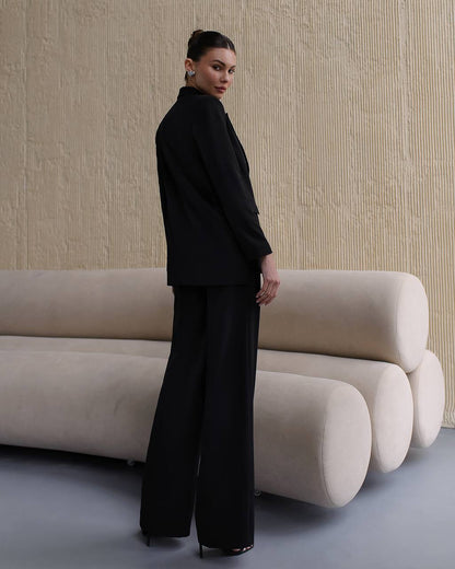 Woman in a black outfit standing in front of a modern beige sofa against a textured wall.
