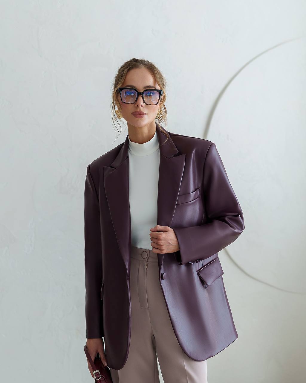 Woman wearing a purple blazer and glasses against a light background