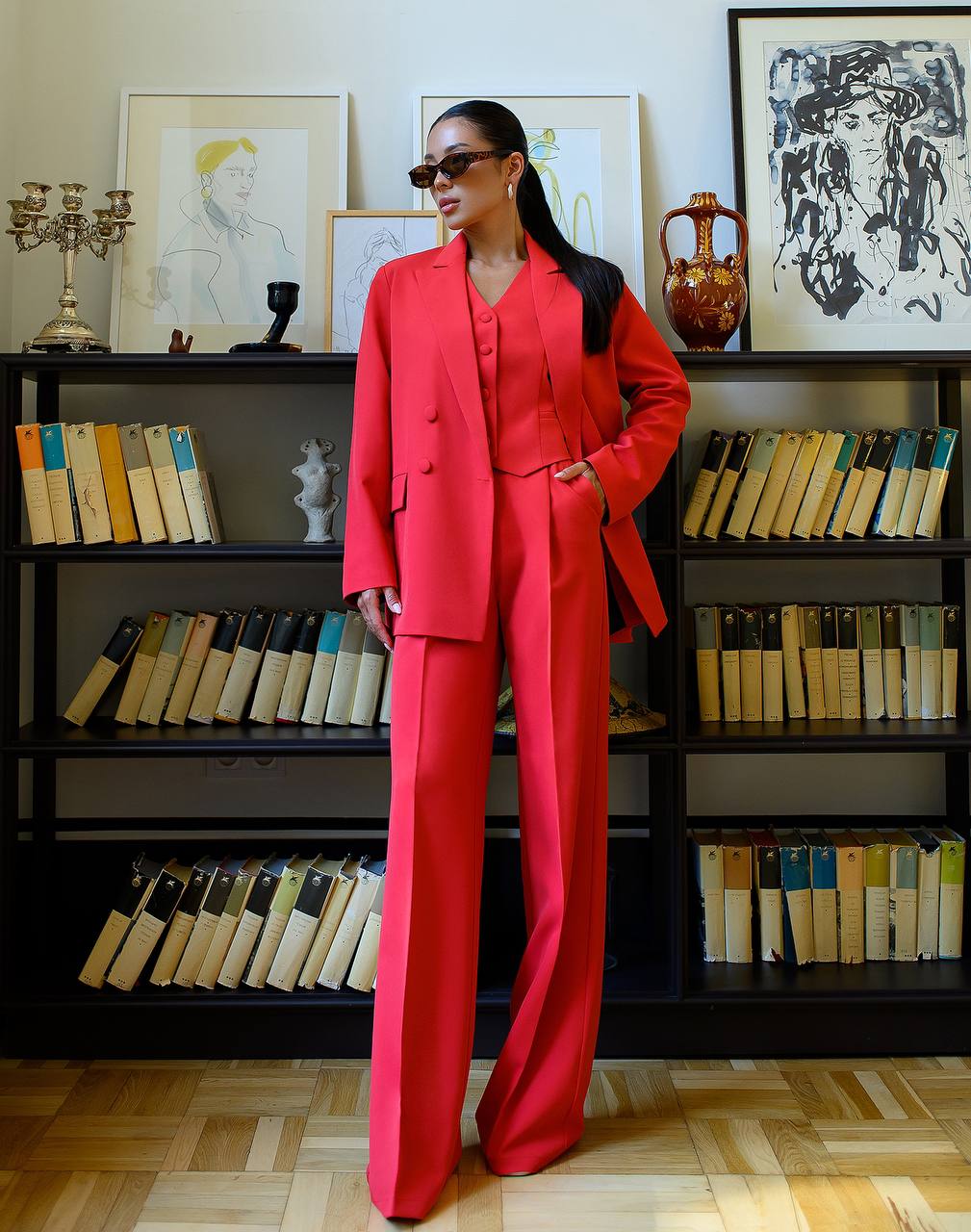Person wearing a red suit standing in front of a bookshelf with books and decorative items.