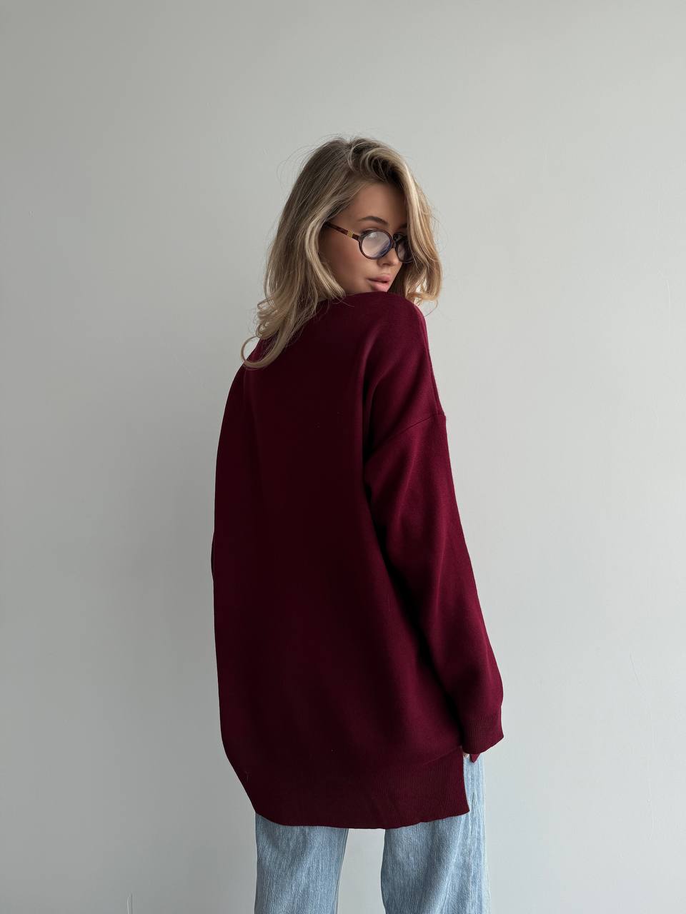 Person wearing a burgundy sweater and light blue jeans against a plain background