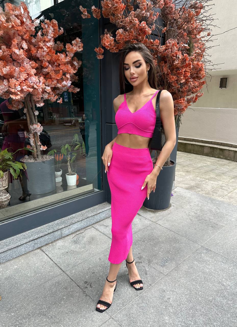 Woman in a bright pink outfit standing on a street with decorative plants.