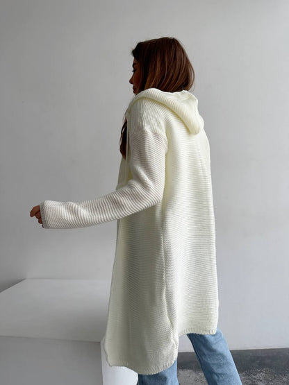 Person wearing a long cream cardigan in a minimalistic setting