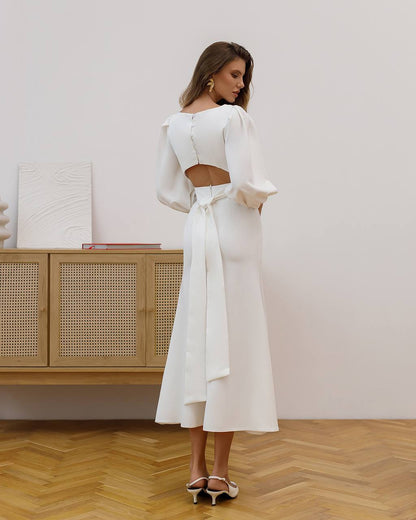 Woman in a white outfit standing in a room with wooden flooring and a wooden cabinet.
