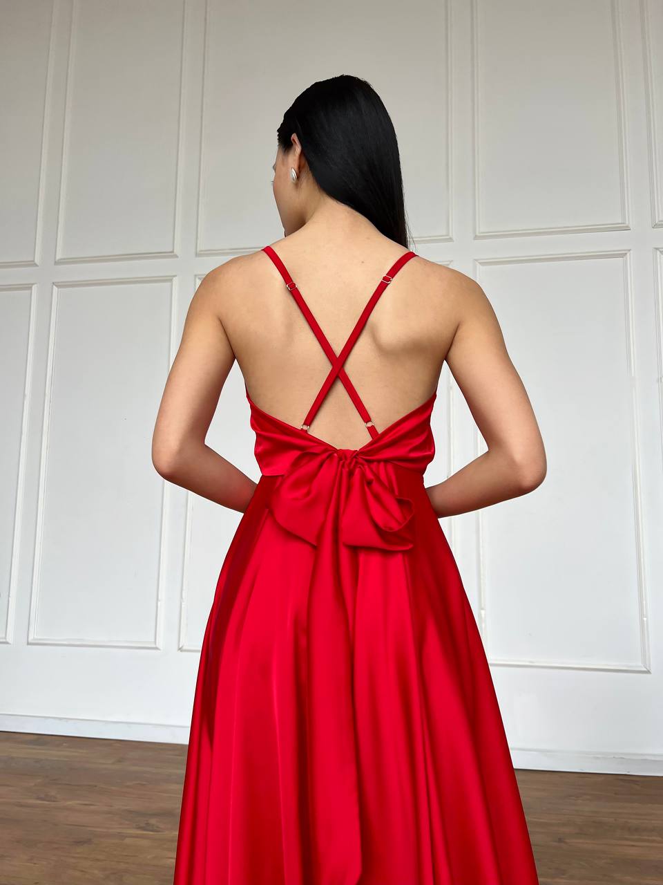 Woman wearing a red dress with a backless design against a white paneled wall.