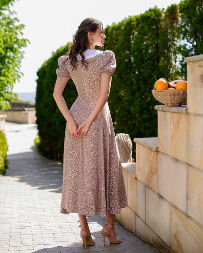 Woman in a patterned dress standing outdoors near stone steps and greenery
