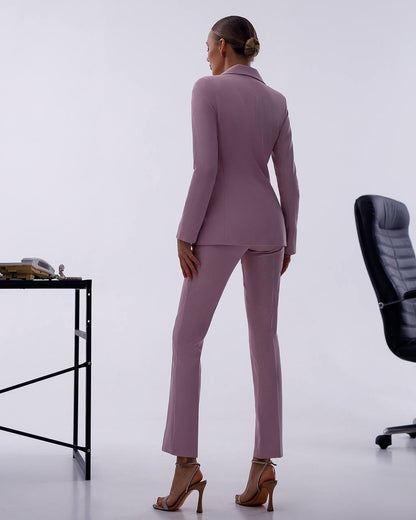 Woman in a mauve suit standing in an office setting with a chair and desk.