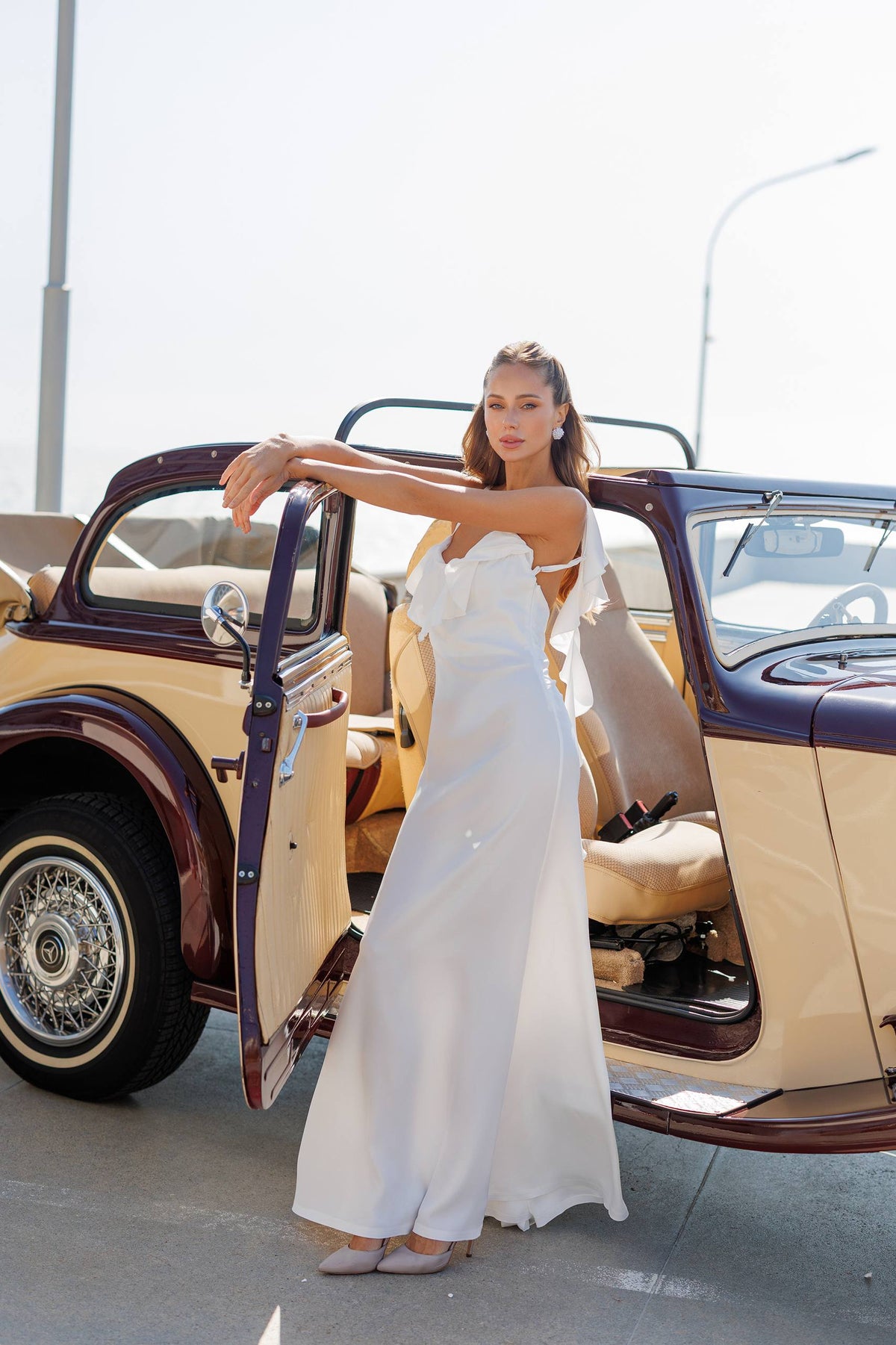 Woman in a white dress standing next to an open vintage car
