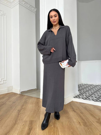 Woman in a gray outfit standing in a room with wooden flooring and white walls.