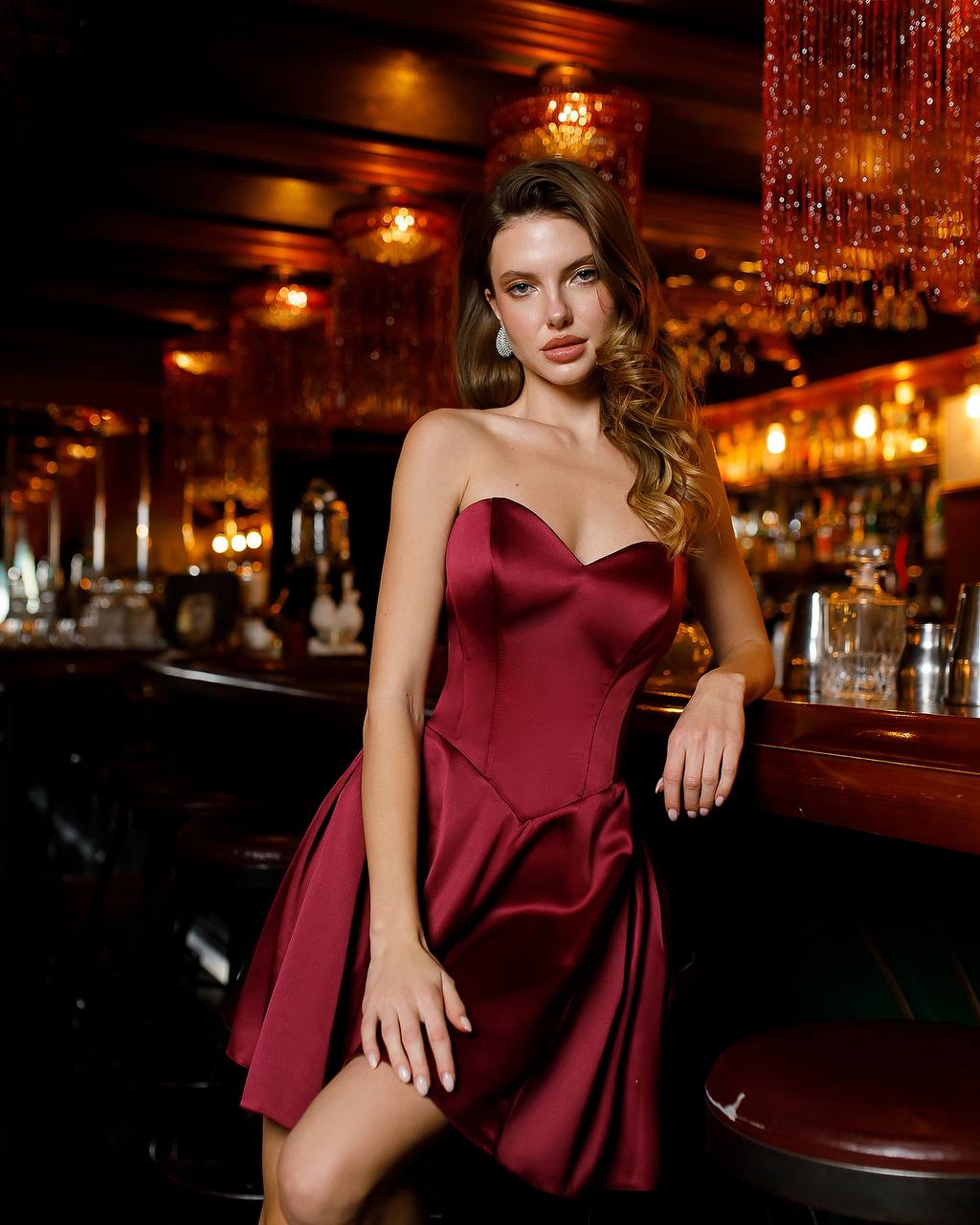 Woman in a burgundy dress sitting at a bar with warm lighting