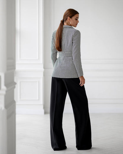 Woman wearing a black and white checkered blouse and black pants in a minimalistic setting