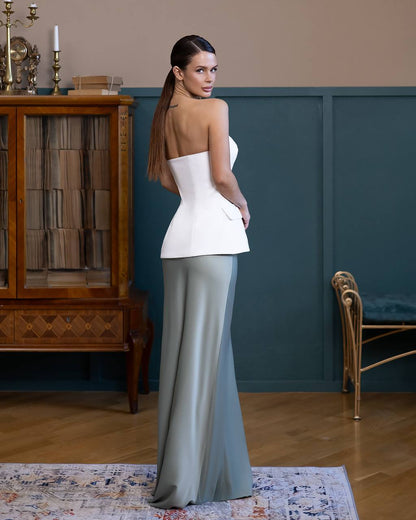 Woman in a white top and gray skirt standing in a room with a wooden cabinet and blue wall.