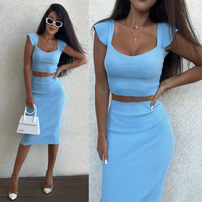 Woman wearing a blue two-piece outfit with a white handbag against a neutral background