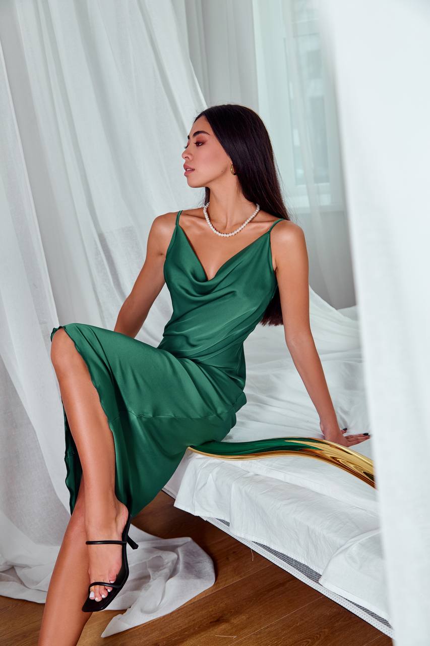 Woman in a green dress sitting on a bed with white curtains in the background