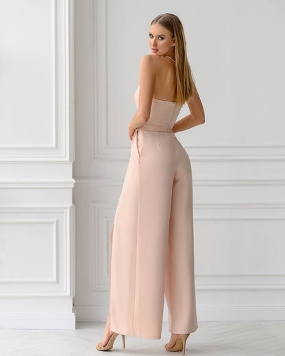 Woman wearing a pink jumpsuit standing against a white wall.