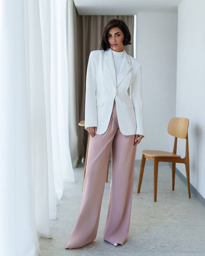 Woman wearing a white blazer and pink pants in a minimalistic room.