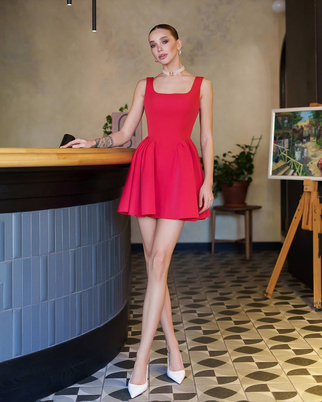Woman in a red dress standing in an indoor setting with a checkered floor.