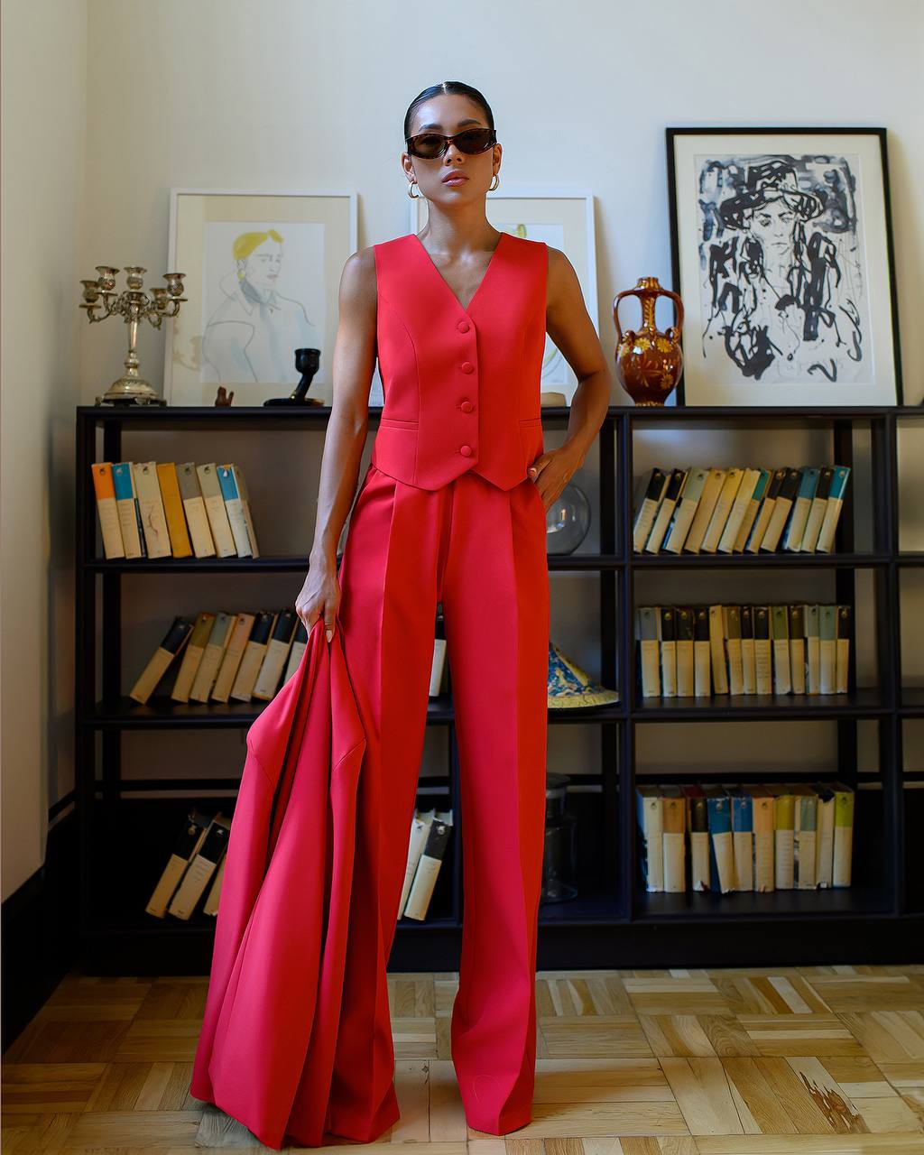Person wearing a red outfit standing in front of a bookshelf with books and decorative items.