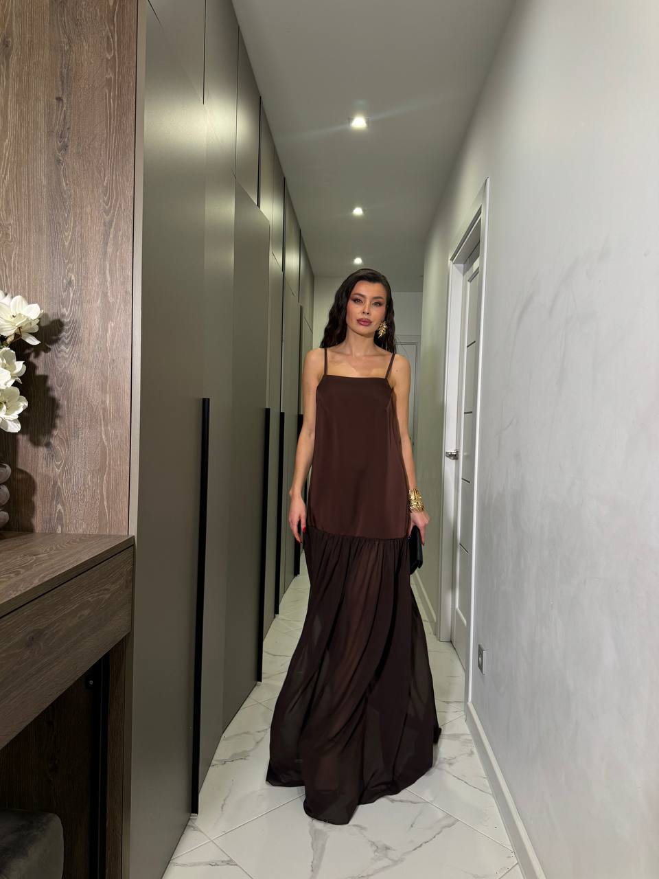Woman in a long brown dress standing in a modern hallway.