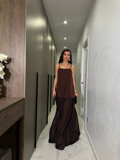 Woman in a long brown dress standing in a modern hallway.