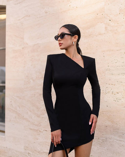 Woman wearing a black dress and sunglasses against a beige wall.