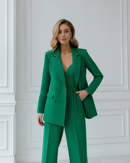 Woman wearing a green suit standing against a white paneled wall.