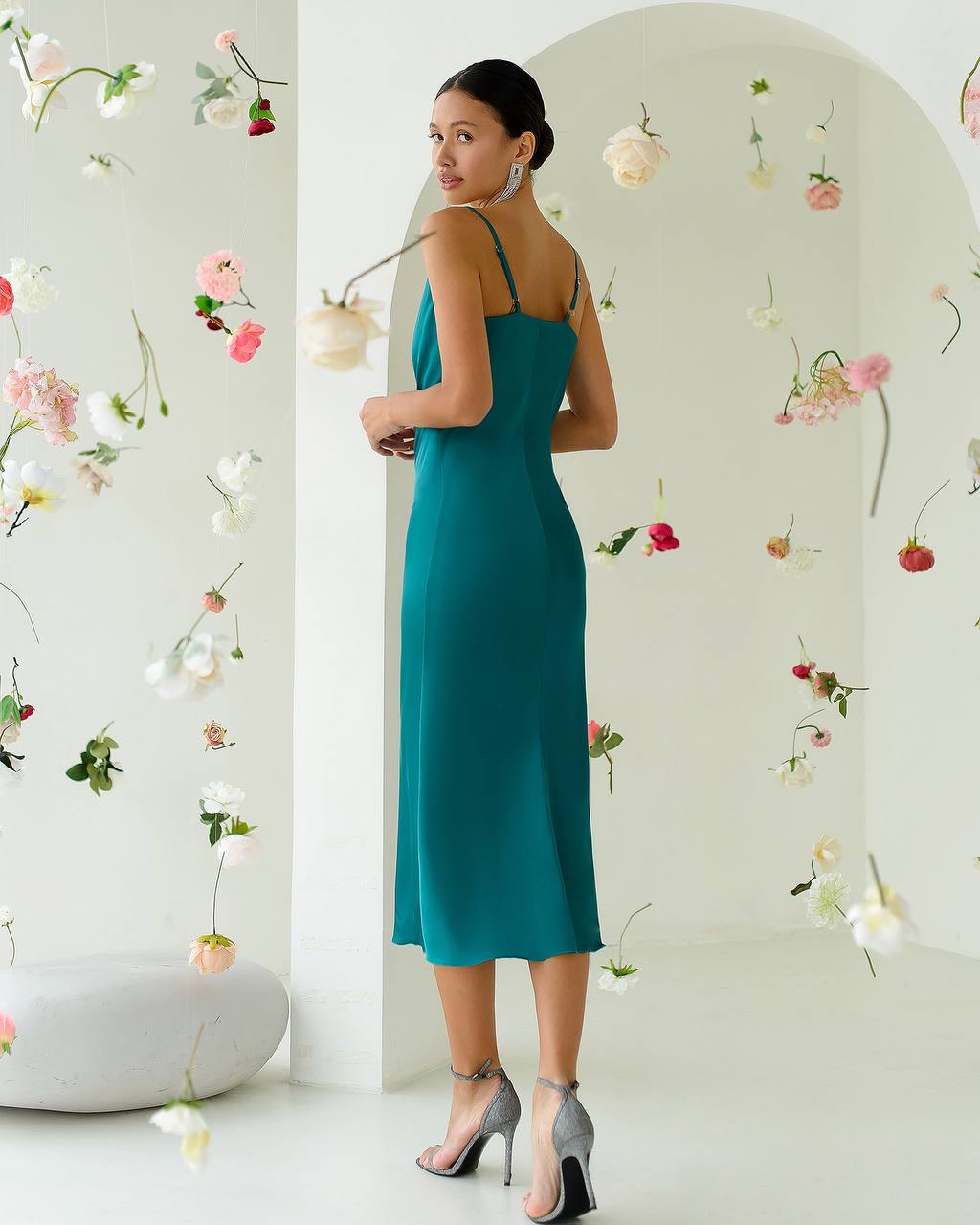 Woman in a teal dress standing in front of a floral wall