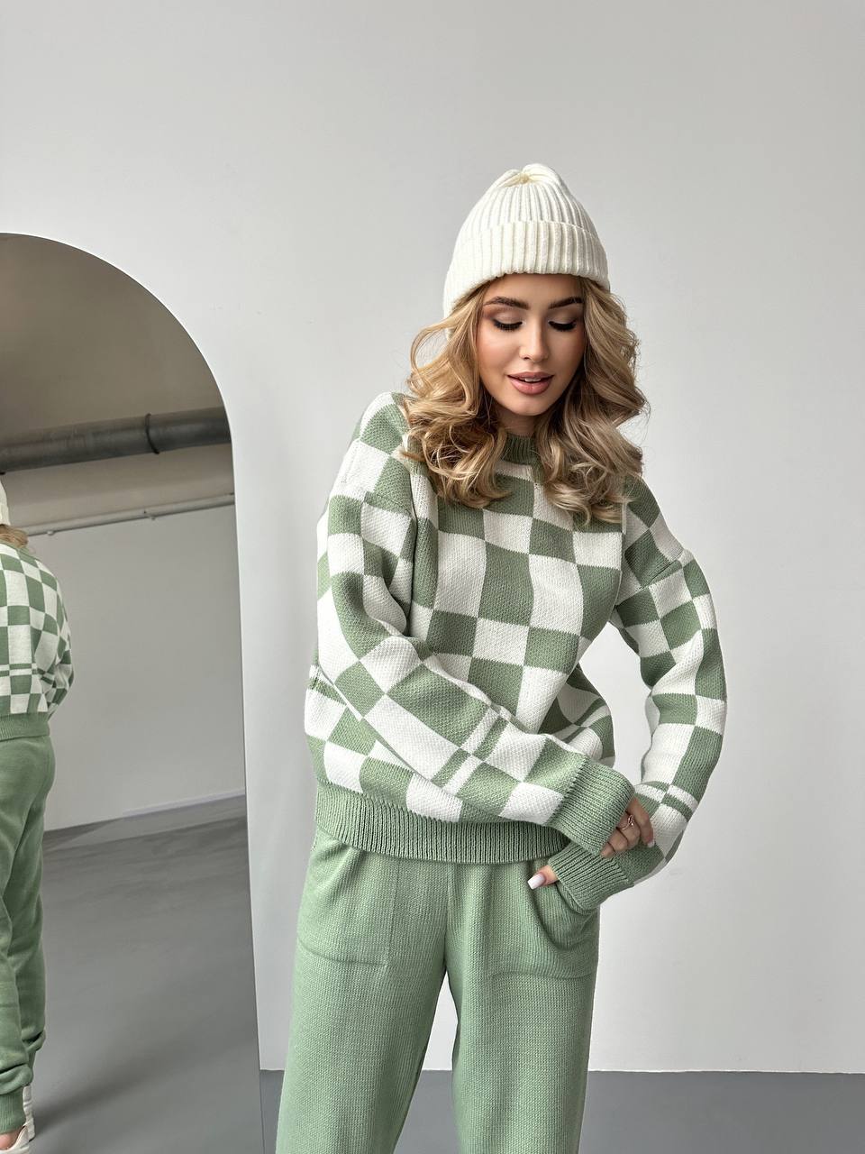 Woman wearing a green and white checkered sweater and pants set with a white beanie.