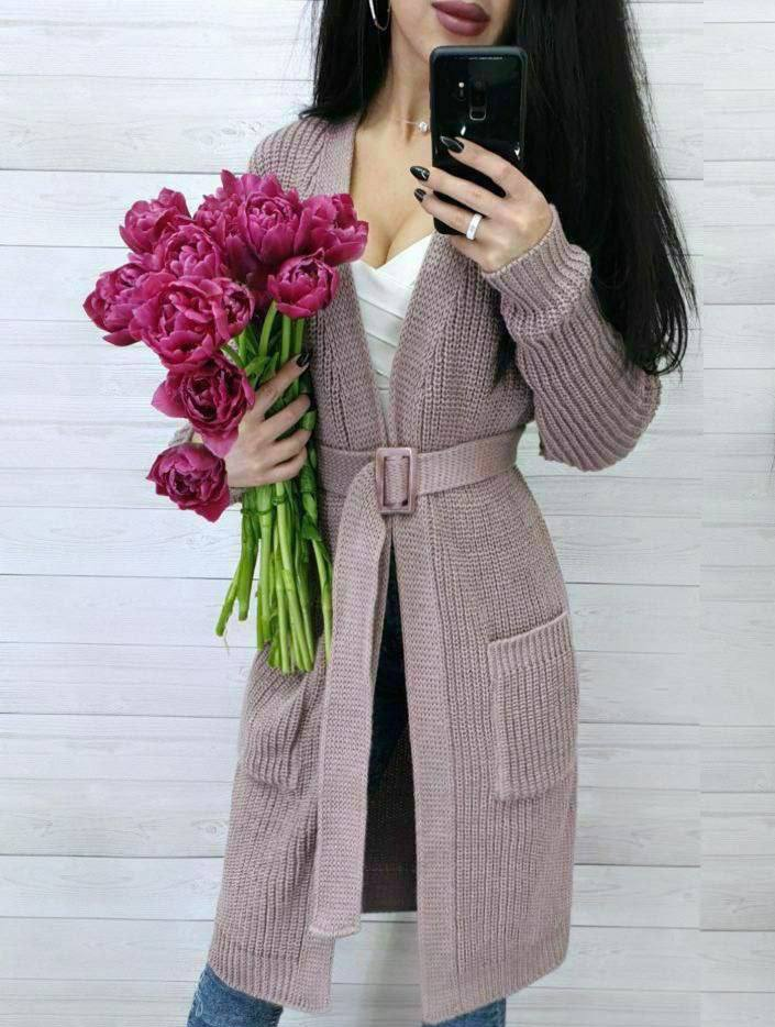 Woman wearing a pink knitted coat holding pink flowers against a white background