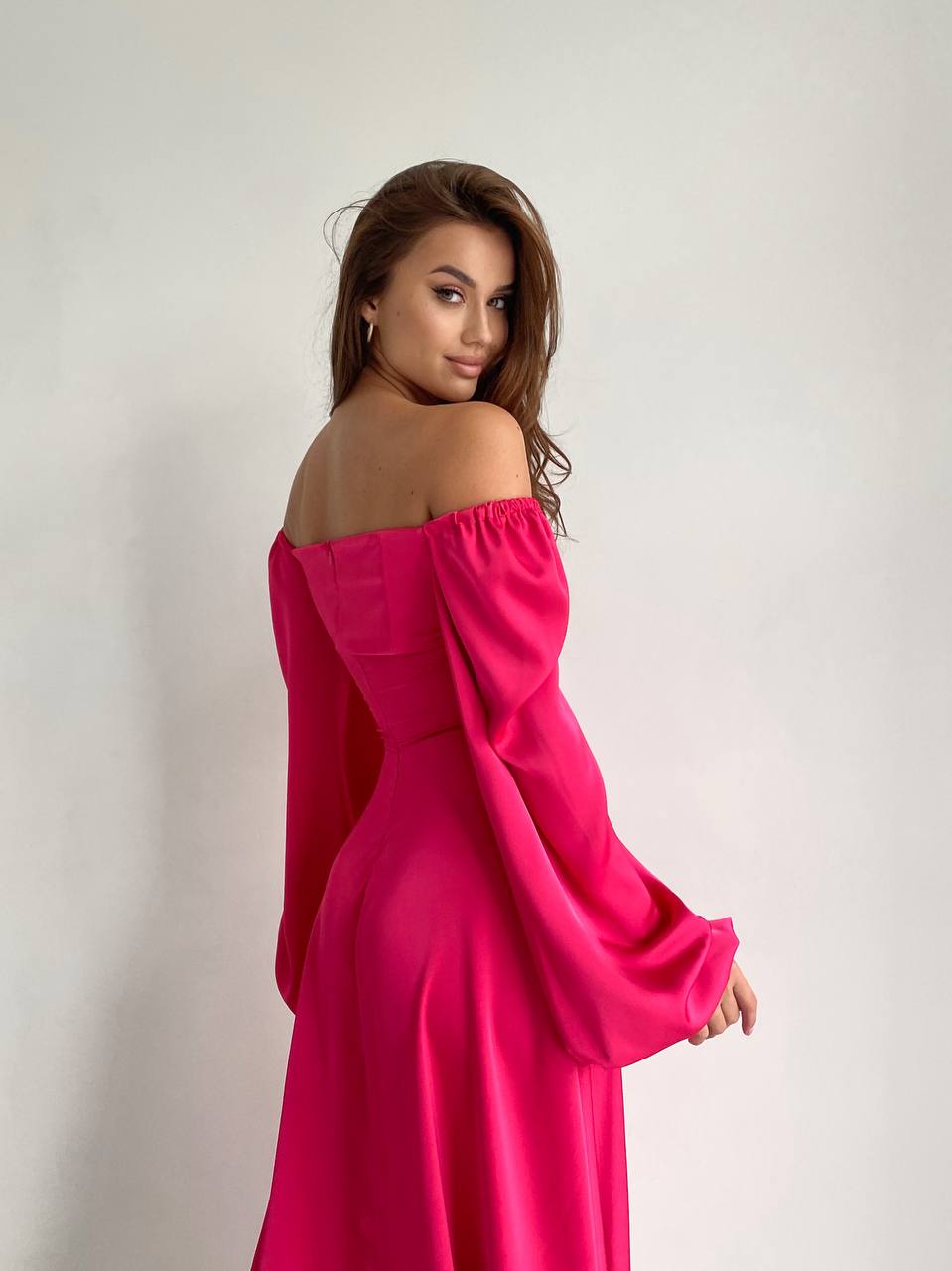 Woman wearing a pink off-shoulder dress against a plain background