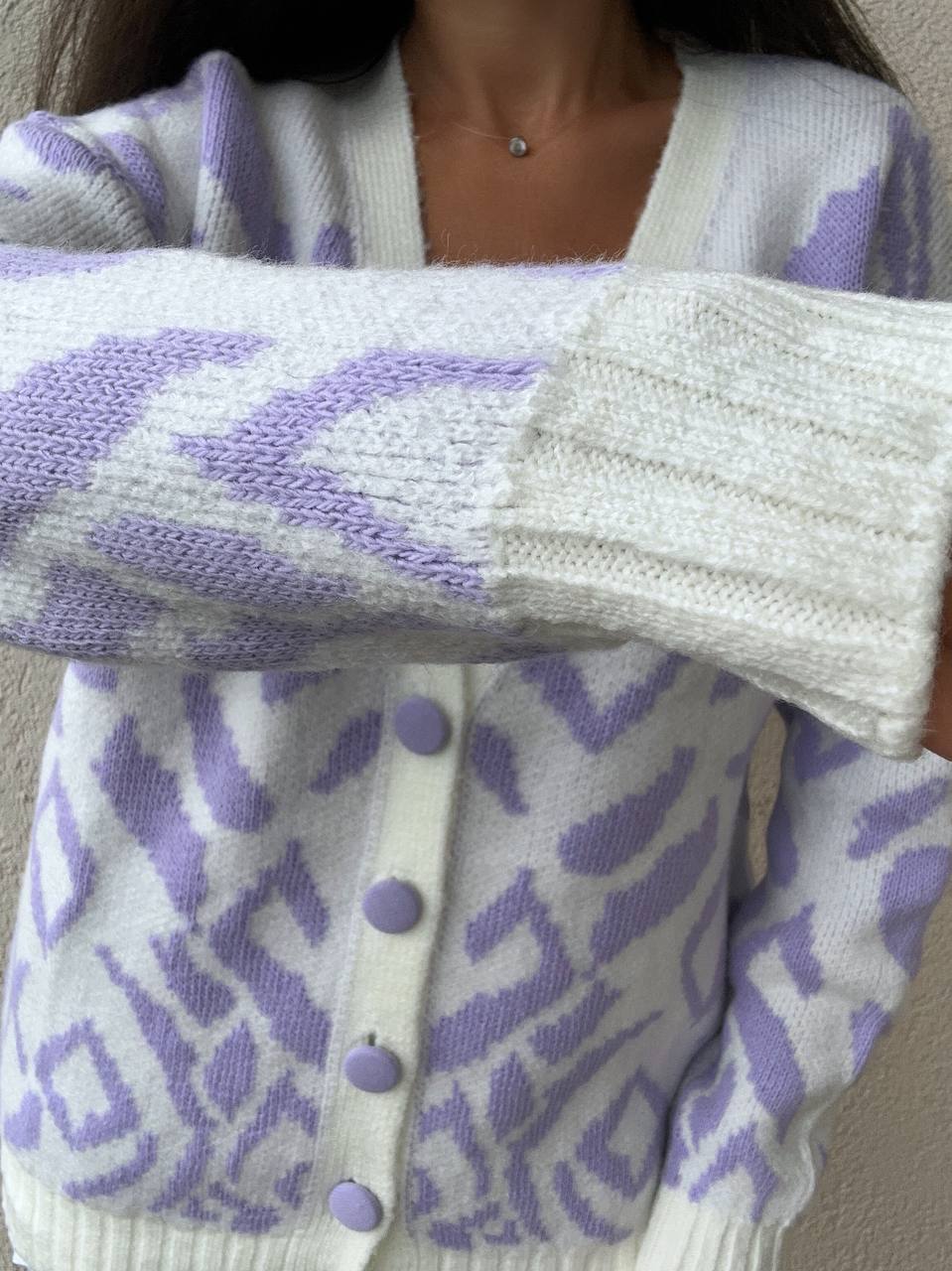 Close-up of a person wearing a white cardigan with purple patterns and buttons.
