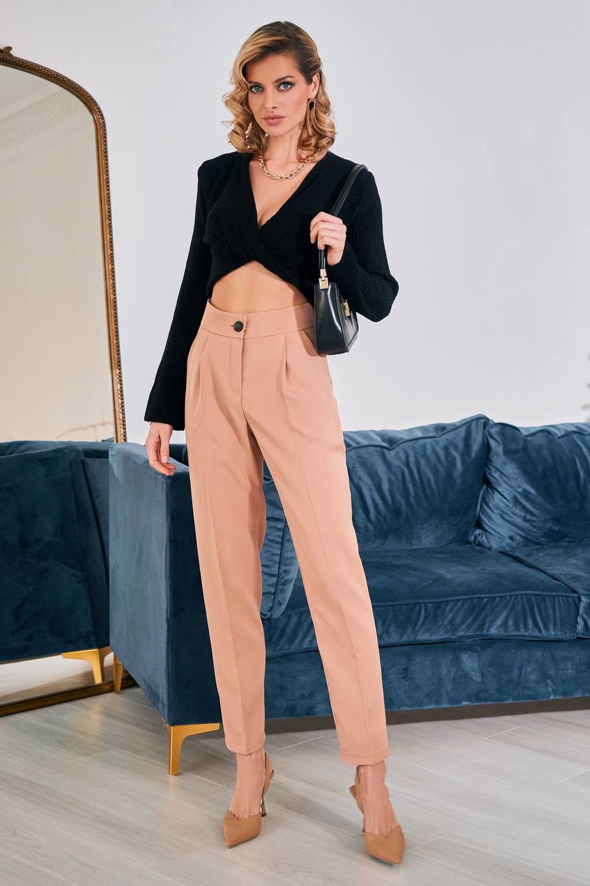 Woman in black blazer and beige pants holding a handbag in a room with a blue couch.