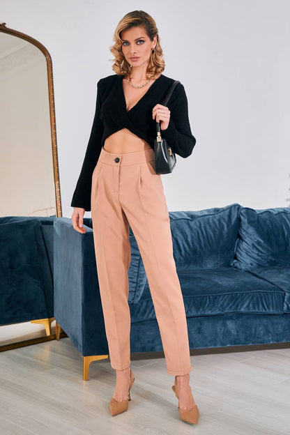 Woman in black blazer and beige pants holding a handbag in a room with a blue couch.
