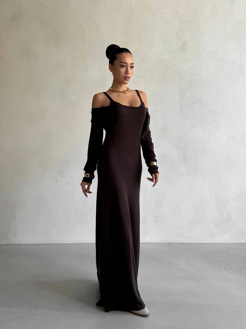 Woman wearing a long dark brown dress against a plain background