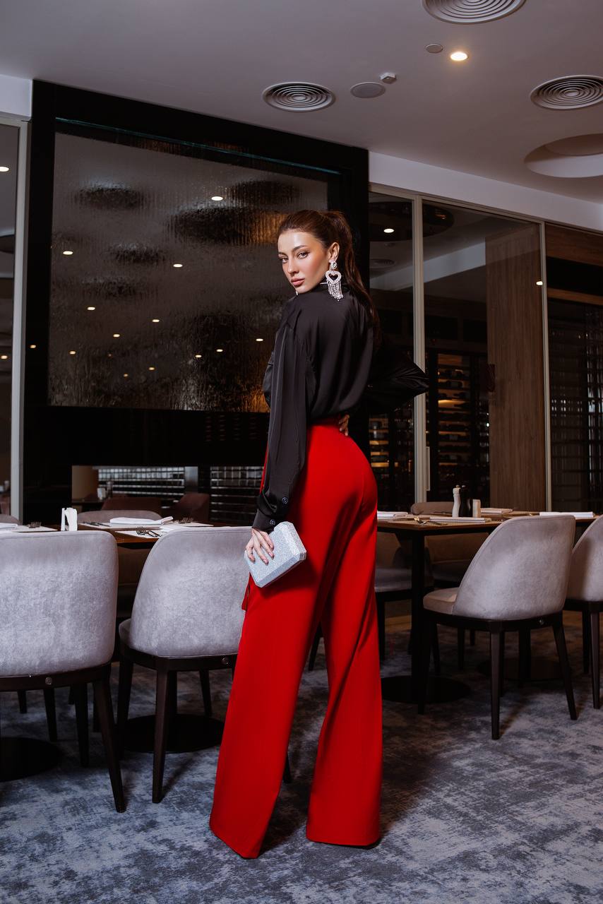 Woman in a black top and red pants standing in a restaurant.