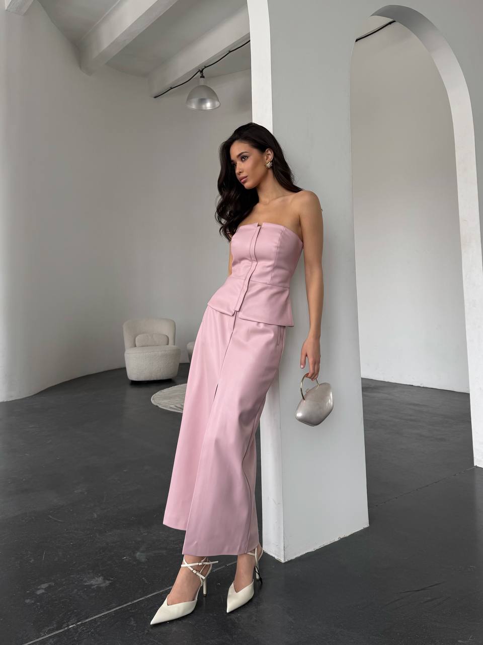 Woman in a pink strapless top and pants standing in a modern interior setting.
