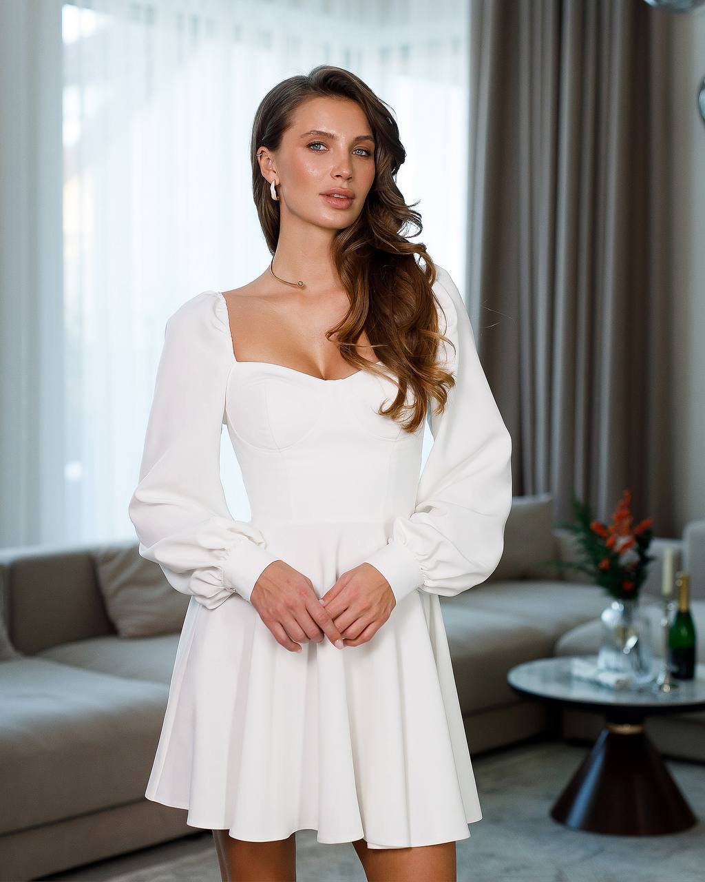 Woman wearing a white dress standing in a living room.
