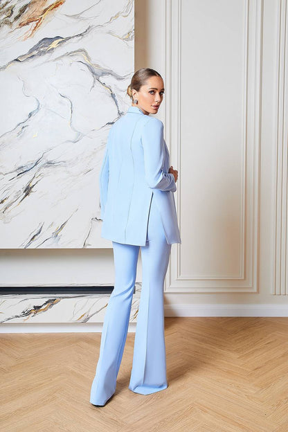 Person wearing a light blue suit standing in a room with marble wall and wooden floor.