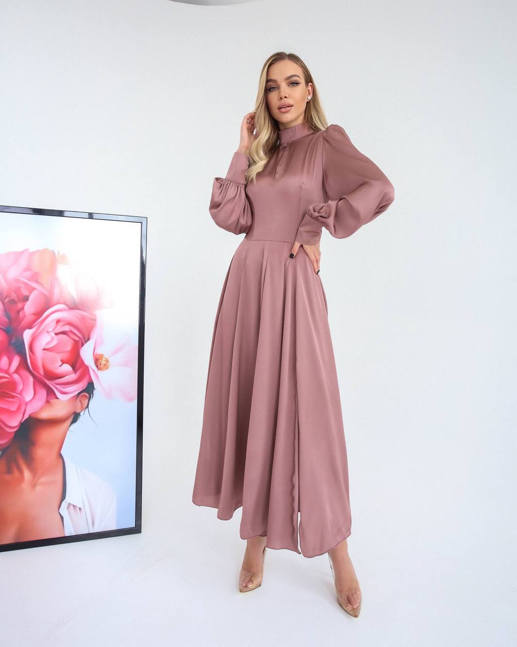 Woman wearing a pink dress standing in front of a framed picture on a white background