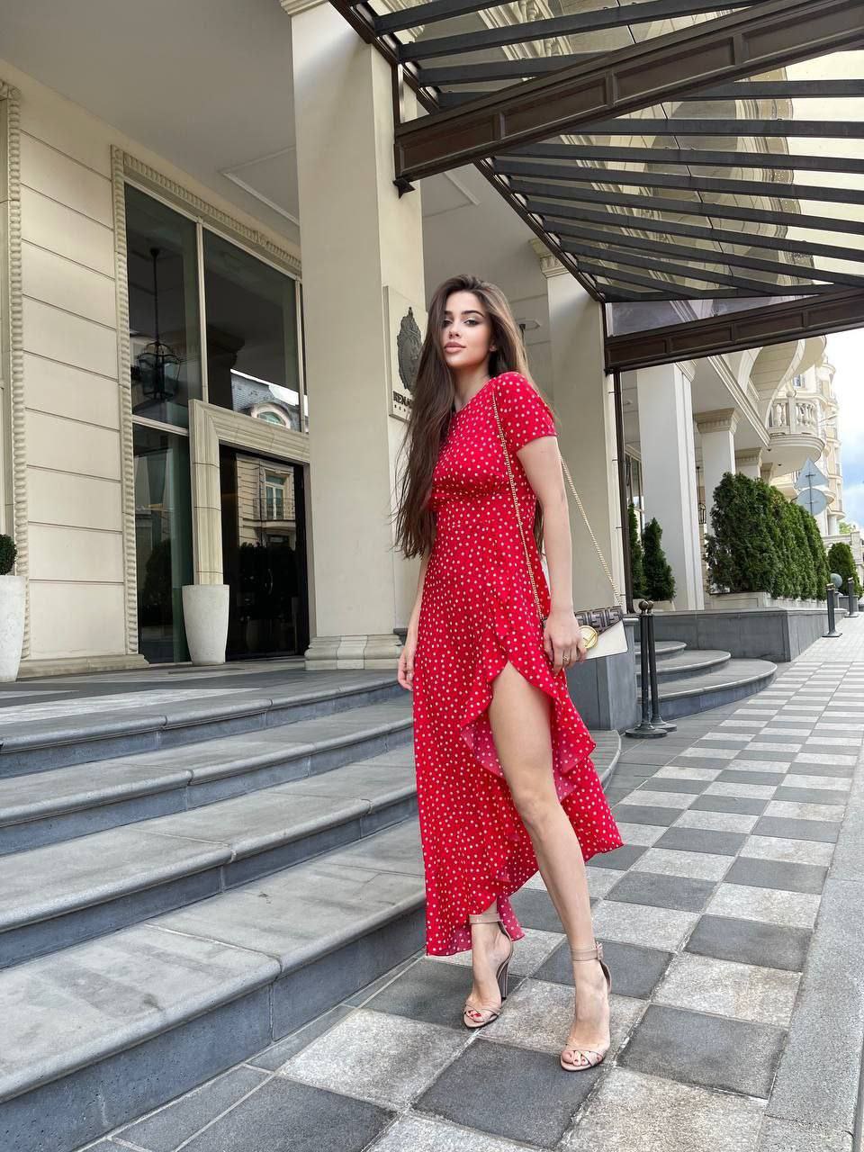 Woman in a red dress standing on a checkered pavement outside a building.