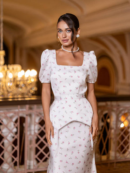 Woman in a white floral dress standing in an elegant indoor setting with chandeliers.