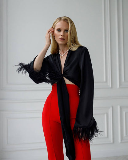 Woman wearing a black top with fringes and red pants against a white paneled wall.