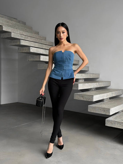Woman in a blue strapless top and black pants standing on concrete stairs.