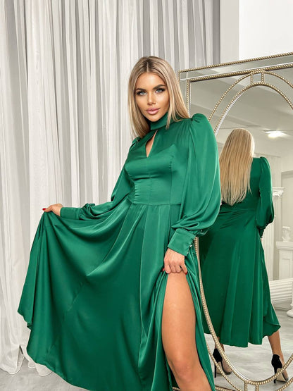 Woman wearing a green dress with a slit, standing in front of a mirror.